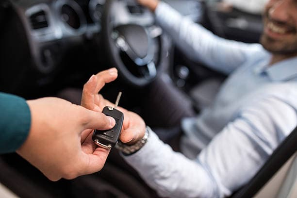 Imagem de um homem de mão estendida recebendo sua chave automotiva modelo canivete sentado no seu automovel